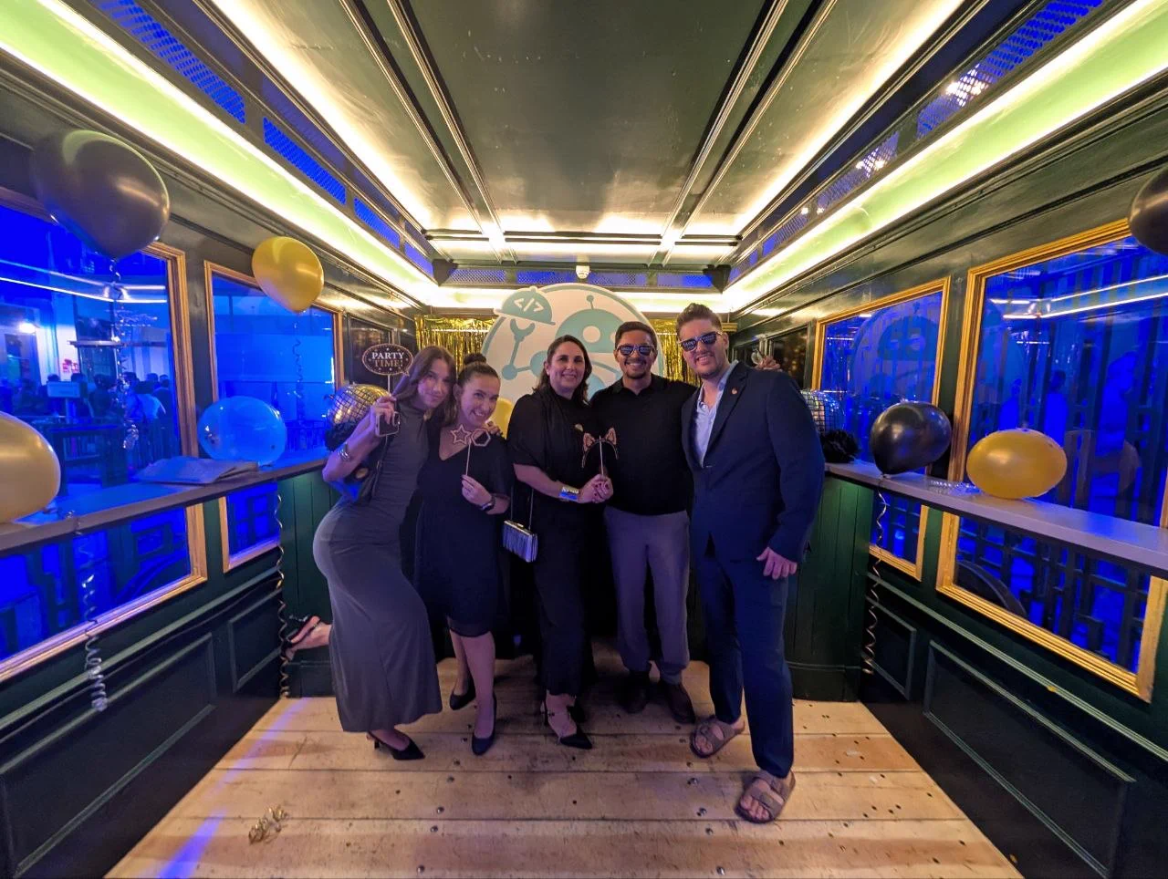 Fotografía de cuerpo entero en un photocall festivo de la gala con globos decorativos. De izquierda a derecha posan sonrientes Aymara Sánchez, María Soria, María Blé, Mario Pinto y Cristian Suárez vistiendo elegantes y sosteniendo accesorios de fiesta.