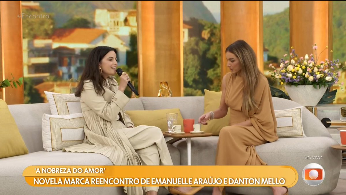 A daytime talk show scene on 'Encontro' with text 'A NOBREZA DO AMOR' and 'NOVELA MARCA REENCONTRO DE EMANUELLE ARAÚJO E DANTON MELLO', showing two women seated on a couch in conversation.