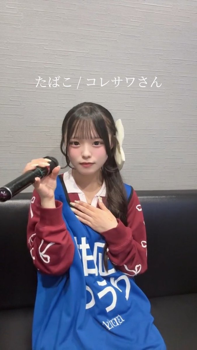 A selfie-style photo of a young woman holding a microphone, wearing a blue and maroon oversized shirt, with Japanese text overlay reading 'たばこ / コレサワさん'.