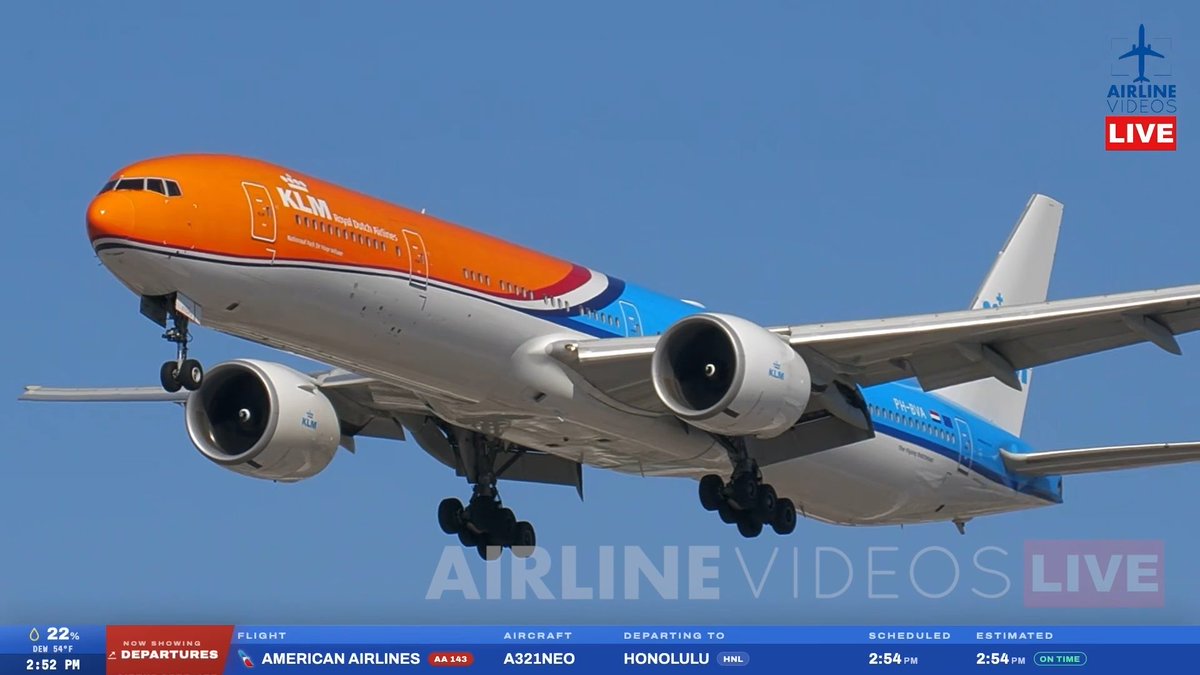 KLM's Boeing 777-300ER "Orange Pride" special livery aircraft lands at LAX on a sunny day, captured on Airline Videos Live. The on-screen graphics show an American Airlines A321NEO departing to Honolulu as flight 603, while the orange KLM jet glides with landing gear extended against a clear blue sky.