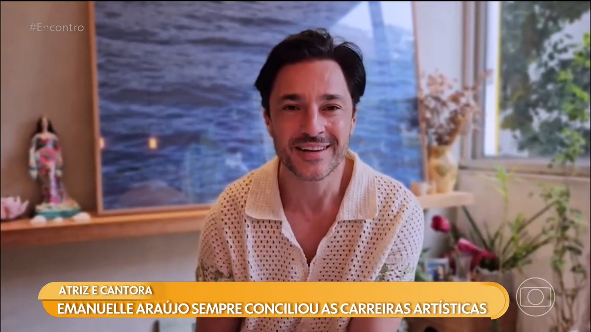 A man in a white knitted shirt is being interviewed on the Brazilian TV show "#Encontro", with a banner reading "ATRIZ E CANTORA EMANUELLE ARAÚJO SEMPRE CONCILIOU AS CARREIRAS ARTÍSTICAS".