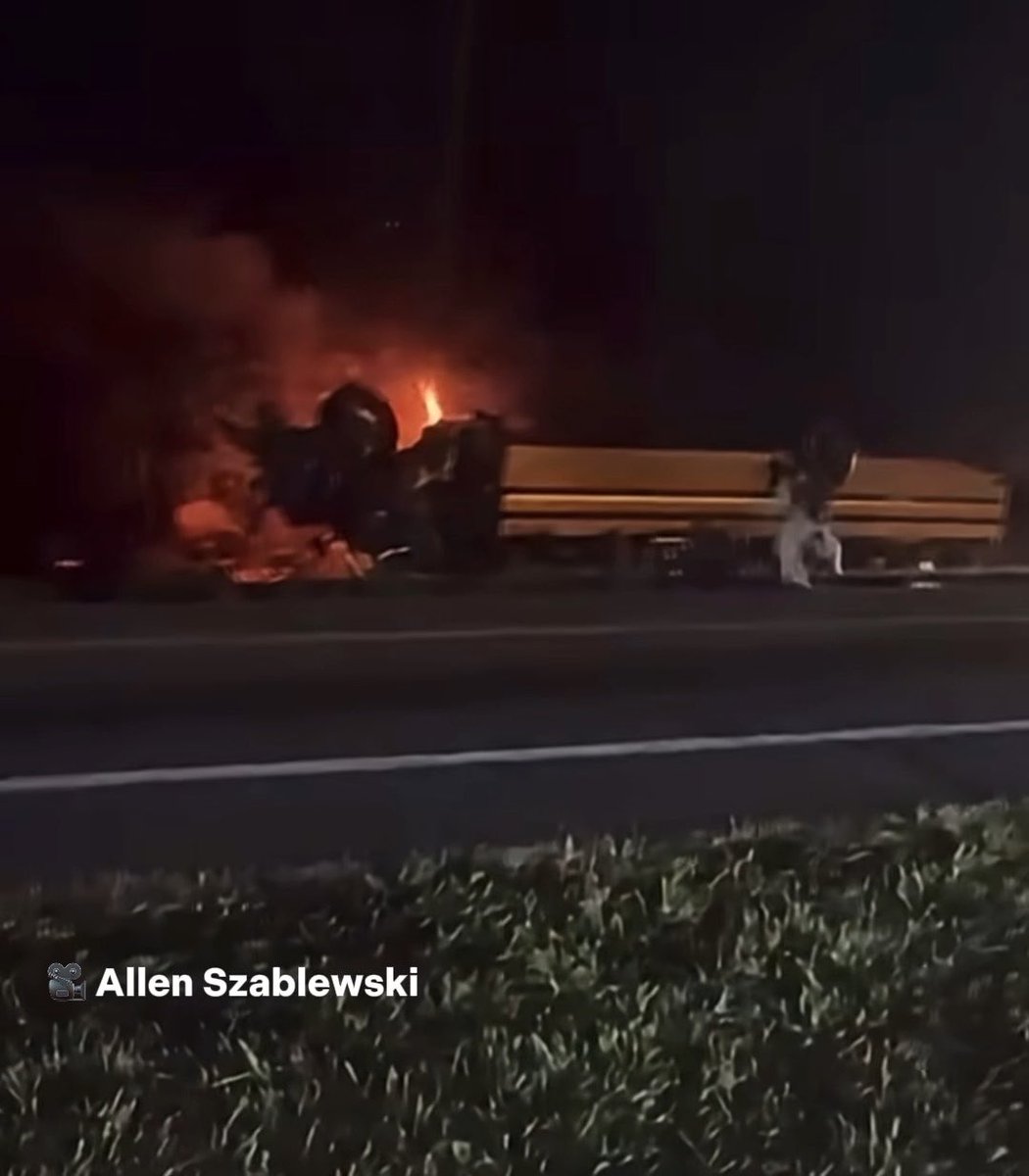 A nighttime photo credited to "Allen Szablewski" shows a school bus engulfed in flames and wreckage on the shoulder of a road, illustrating the fatal multi-vehicle crash in Winter Haven that left two people dead and dozens more injured.