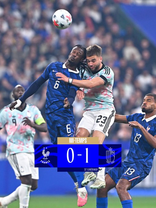 The image captures an intense aerial duel between a French player (#6) and a Belgian player (#23) during a soccer match, with another Belgian player (#9) and French player (#13) in the background. A scoreboard overlay shows "MI-TEMPS" (halftime) with a 0-1 scoreline, confirming France trails Belgium 1-0 at the break, matching the caption's note that there's still 45 minutes left for France to "turn the tide."