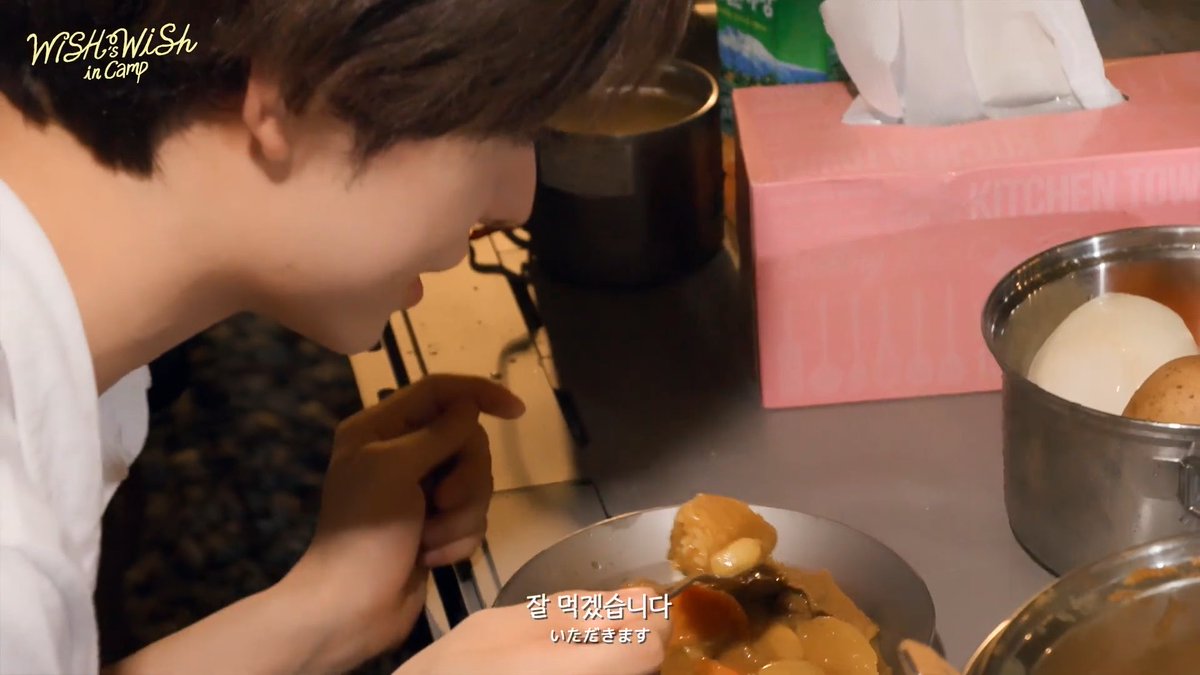 A young child prepares to eat a meal from a metal plate at a table, with the text 'WISH in Camp' in the upper left and Korean subtitles '잘 먹겠습니다' and 'いただきます' at the bottom.