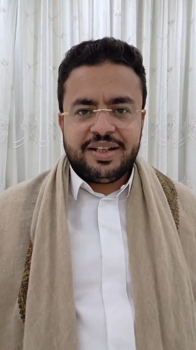 A bearded man wearing glasses and a white shirt with a beige shawl speaks directly to the camera against a white curtain backdrop. The image accompanies a post asking "What is really happening and where are things heading?!" suggesting he is delivering an explanatory or clarifying video message.