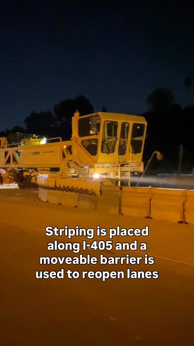 A yellow construction vehicle works on a road at night, with text overlay stating 'Striping is placed along I-405 and a moveable barrier is used to reopen lanes.'