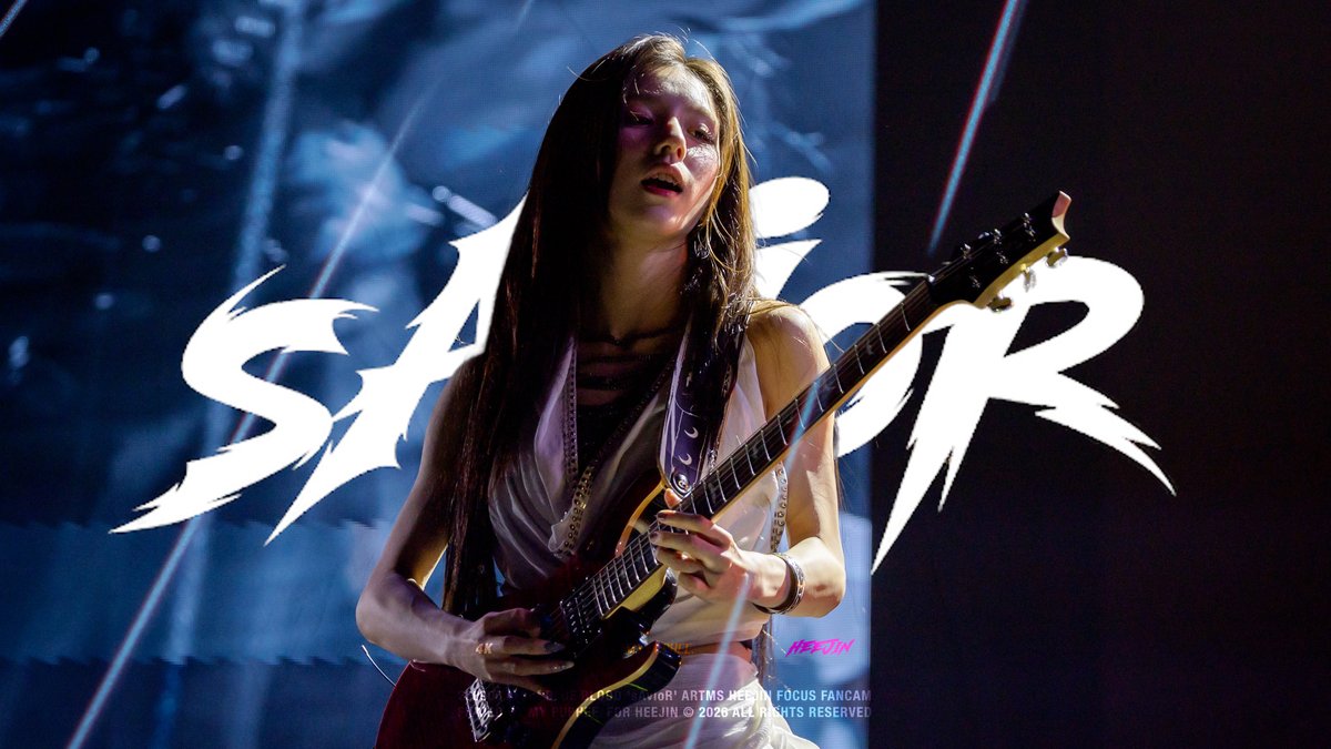 A female guitarist performs on stage in front of a backdrop with large stylized lettering, with small text noting 'LEADERS: HEERIN AR7MS HEERIN FOCUS FANCAM FOR HEEJIN © 2026 ALL RIGHTS RESERVED'.