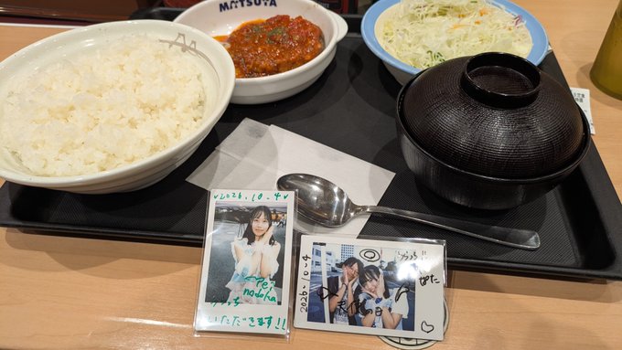 A Japanese meal set at Matsuya featuring a bowl of white rice, meat sauce, cabbage salad, miso soup, and two signed photo cards of an idol group member.