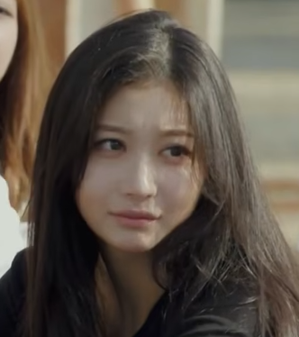 A close-up portrait of a young woman with long dark hair looking slightly off-camera with a soft expression, appearing to be from a Korean drama or music video.