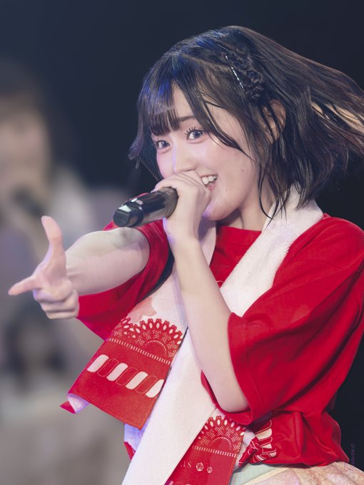A young female performer smiles and points forward, holding it while wearing a red and white outfit.