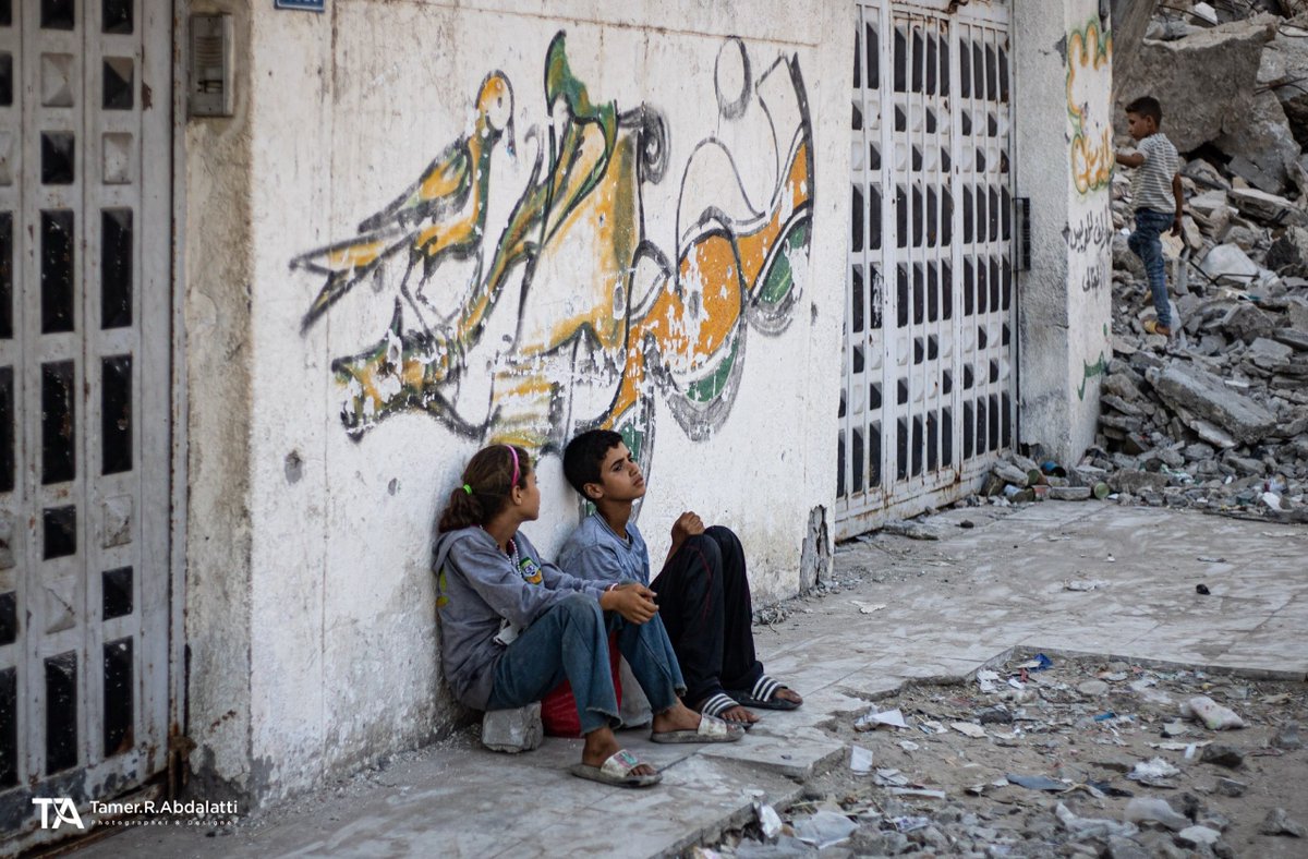 EyeonPalestine's tweet photo. Among the rubble in Gaza, two children sit as if resting from a weight far beyond their years. They are no longer looking for places to play... they are looking for a safe corner to sit, and a moment of peace amid the ruins. This is more than a photograph... it is childhood trying to survive.

أمام الجدران الموشاة بالدمار وفي قلب الركام بغزة، يجلس طفلان كأنهما يستريحان من ثقل يزن أكثر بكثير من سنوات عمرهما. هما لا يبحثان عن مكان للعب، بل عن زاوية آمنة ولحظة سلام وسط الأنقاض. ليست مجرد صورة، بل طفولة تحاول النجاة.