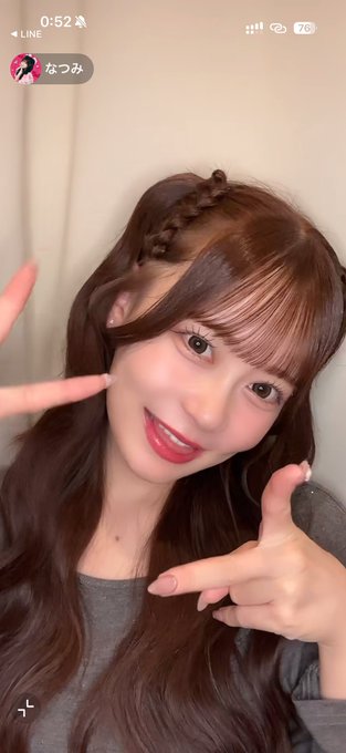 A selfie of a young woman with long brown wavy hair and a braided detail smiles and makes peace signs in a LINE video call, with the username 'なつみ' visible.