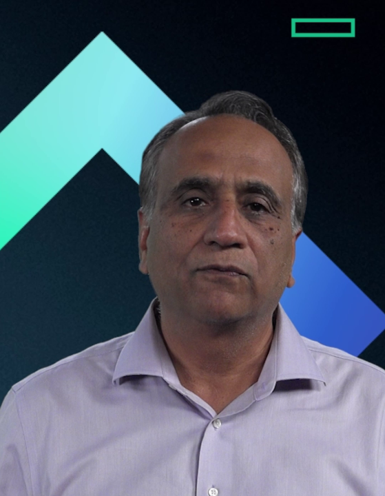 A man with short graying hair wearing a light purple button-up shirt speaks on camera against a dark background with a teal and blue geometric design.