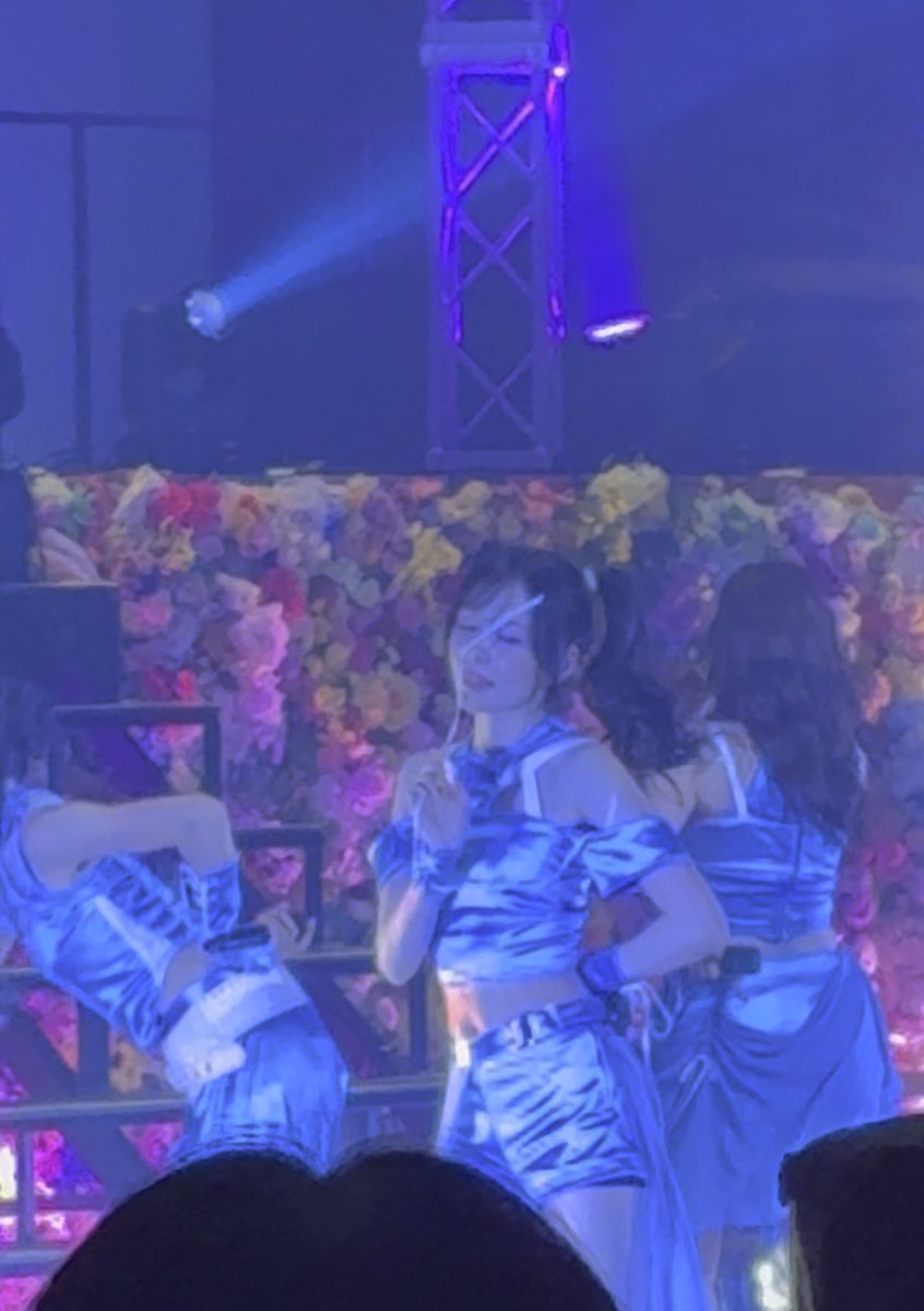 Performers in shiny blue outfits dance on a stage under blue lighting, featuring a backdrop covered in pink and blue blooms.