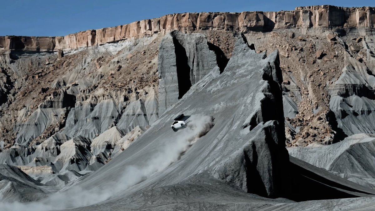 A dramatic landscape featuring a white vehicle kicking up a massive cloud of dust while driving down a steep, gray, rocky ridge or canyon slope against a backdrop of layered, eroded cliffs.
