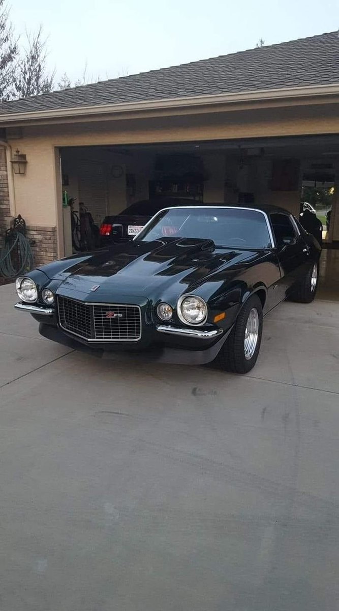 RestoMod804's tweet photo. Chevrolet Camaro Z28 — Dark green with cowl hood breathing, split chrome bumpers, red Z28 badge glowing in mesh grille, chrome deep-dish wheels sitting clean on driveway. https://t.co/QqbD1dACEe