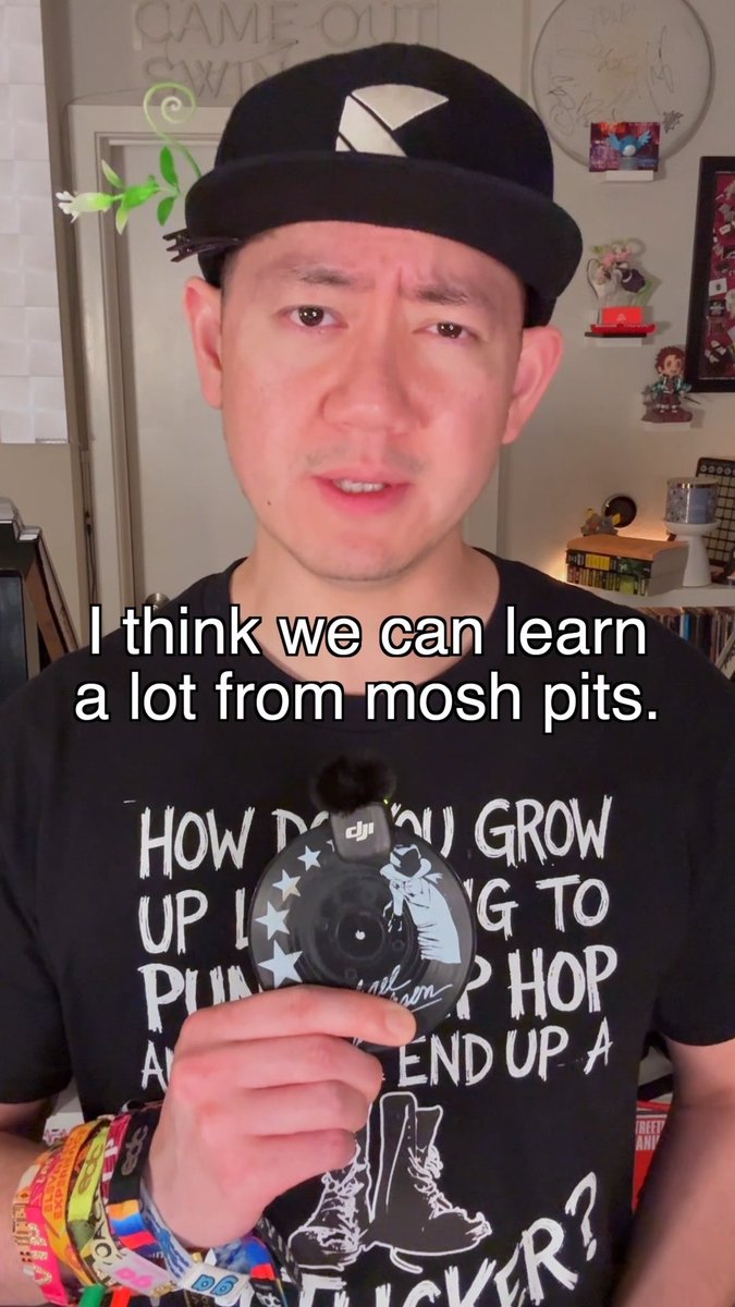 A man wearing a black cap and black t-shirt with white text holds a small circular DJI device, with a caption reading 'I think we can learn a lot from mosh pits.'