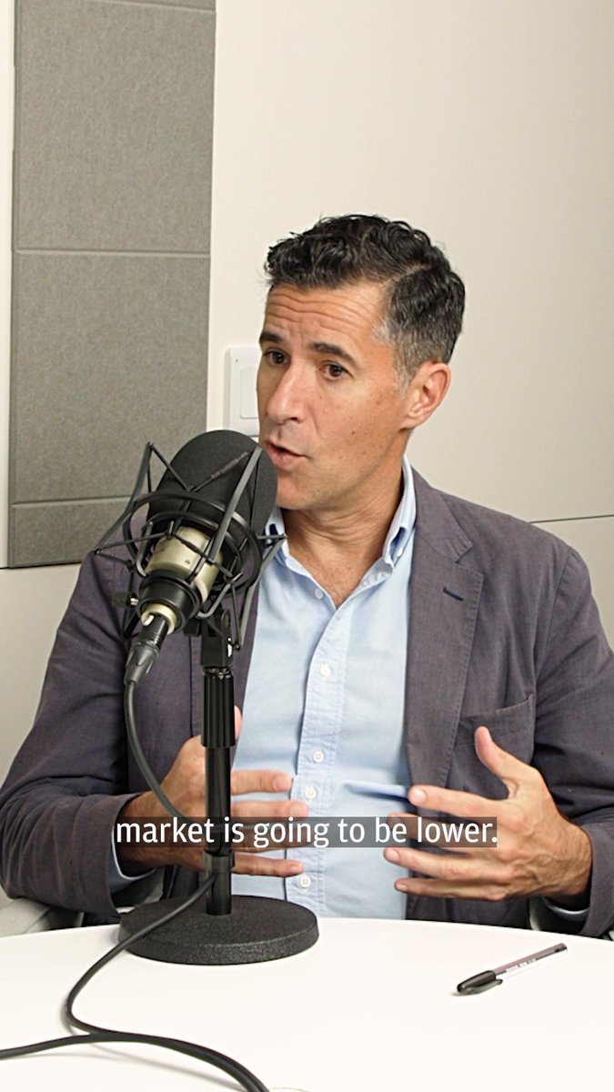 A man in a gray blazer and blue shirt speaks into a studio microphone while gesturing with his hands, with the caption "market is going to be lower." displayed at the bottom, capturing Mike Feroli's podcast appearance discussing the September jobs report's implications for the economy and Federal Reserve policy.