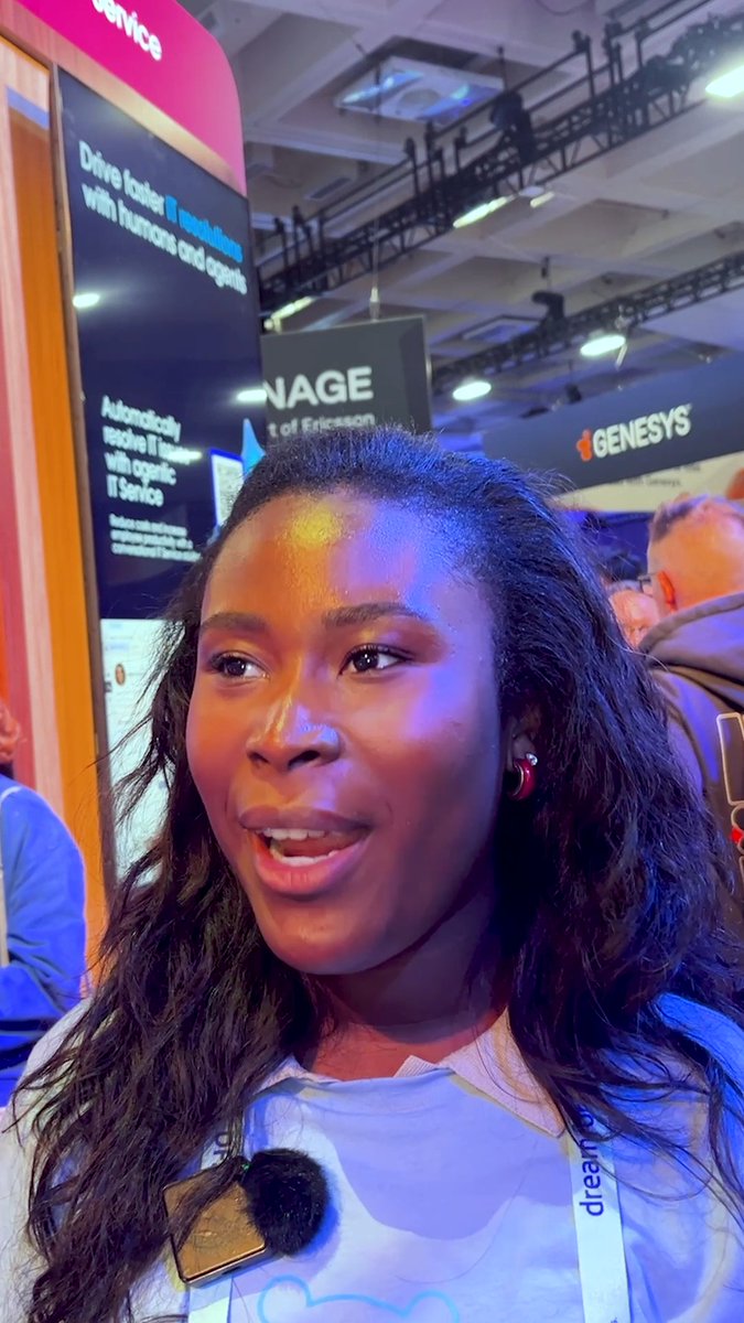 A close-up photo captures a young woman with long dark hair speaking into a microphone at a tech conference, with signage for 'GENESYS' and 'Ericsson' visible in the background.