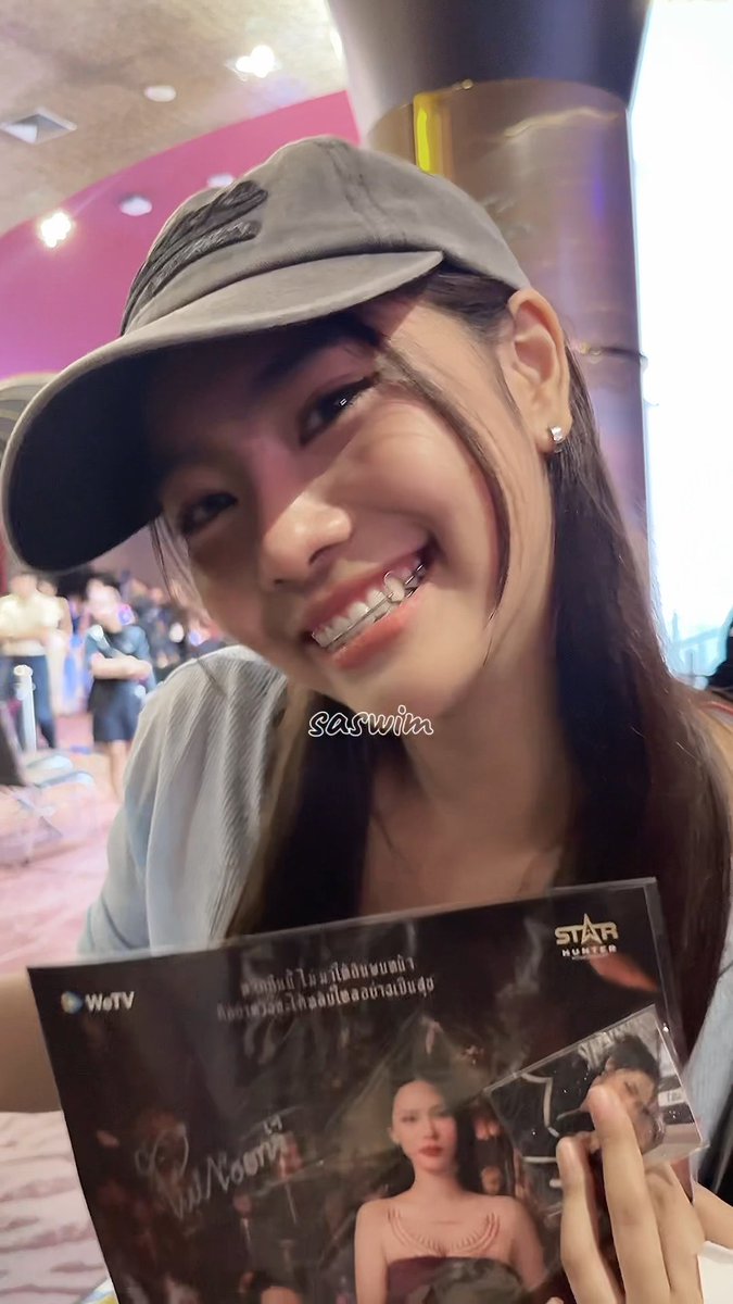 A smiling young woman wearing a black baseball cap and diamond-studded grillz holds what appears to be promotional photos or a fan event item from WeTV and STAR HUNTER; watermark reads 'saswin'.