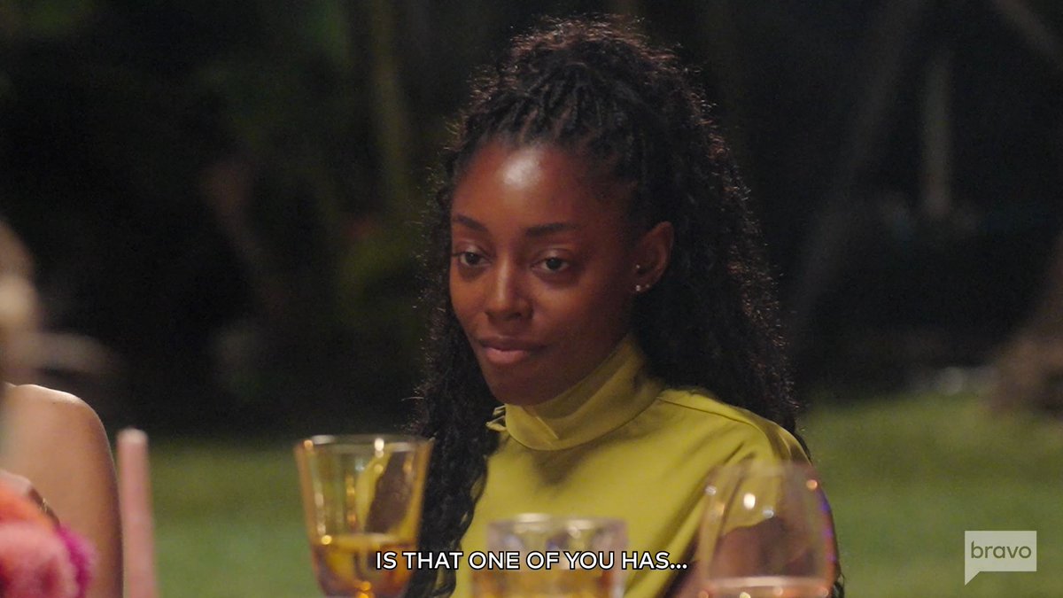 A woman with braided hair sits at an outdoor dinner table in a yellow top, looking contemplative as the subtitle reads "IS THAT ONE OF YOU HAS..." while the Bravo logo appears in the corner. The scene captures a dramatic, tension-filled moment that hints at the confrontations and revelations teased in the new season of Southern Charm.