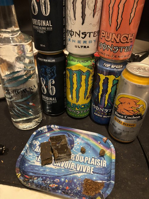 An assortment of alcoholic beverages including vodka, Monster Energy drinks, and beer, arranged alongside a tray with chocolate pieces and what appears to be cannabis.