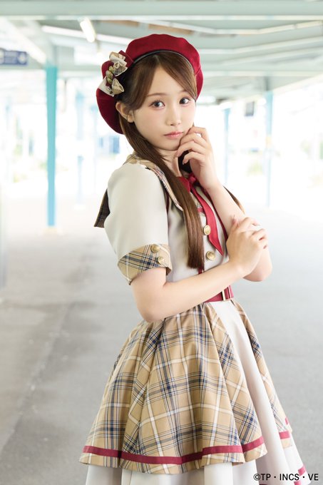 A promotional photo of a young woman wearing a red beret and a plaid cream-colored dress, credited to "TP\incs\ve."
