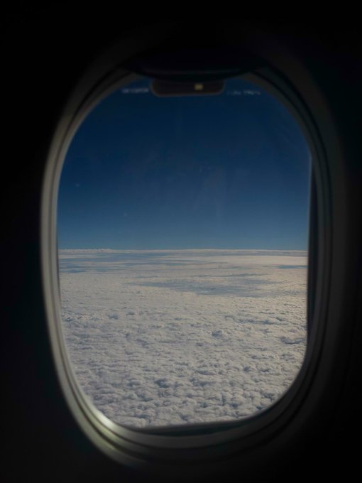 A view through an airplane window showing a vast expanse of clouds beneath a deep blue sky, with no visible text. The image perfectly illustrates the post's sentiment, capturing the stunning natural scenery visible from the rare open window shade the poster is enjoying.