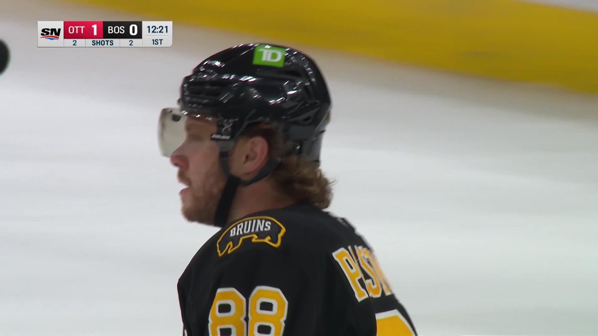 A close-up profile shot of a Boston Bruins hockey player wearing a black helmet with a TD logo and jersey number 88, during a game against Ottawa with the scoreboard showing OTT 1, BOS 0 at 12:21 in the 1st period.