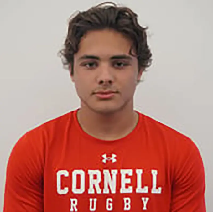 A young man with curly dark hair poses for a headshot wearing a red Cornell Rugby t-shirt with the Under Armour logo visible. The image corresponds to Matthew Ingalls, the Cornell fraternity member referenced in the accompanying post about the alleged incident.