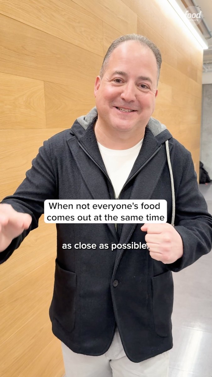 A man in a dark hoodie smiles at the camera, with on-screen text reading, "When not everyone's food comes out at the same time as close as possible."