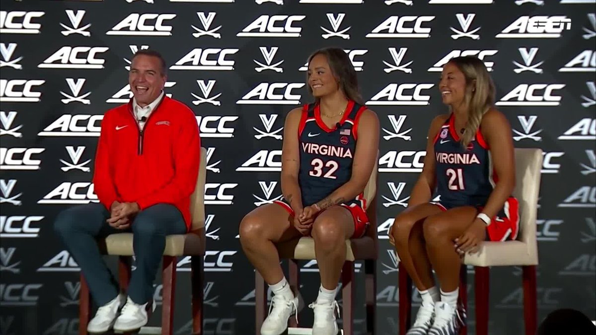 Three people sit on stage at an ACC press conference; a man in red Virginia apparel sits next to two female athletes wearing Virginia basketball jerseys numbered 32 and 21.