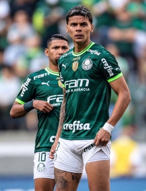 Two soccer players wearing green jerseys featuring 'crefisa' and 'FAM' sponsor logos stand on the field during a match.