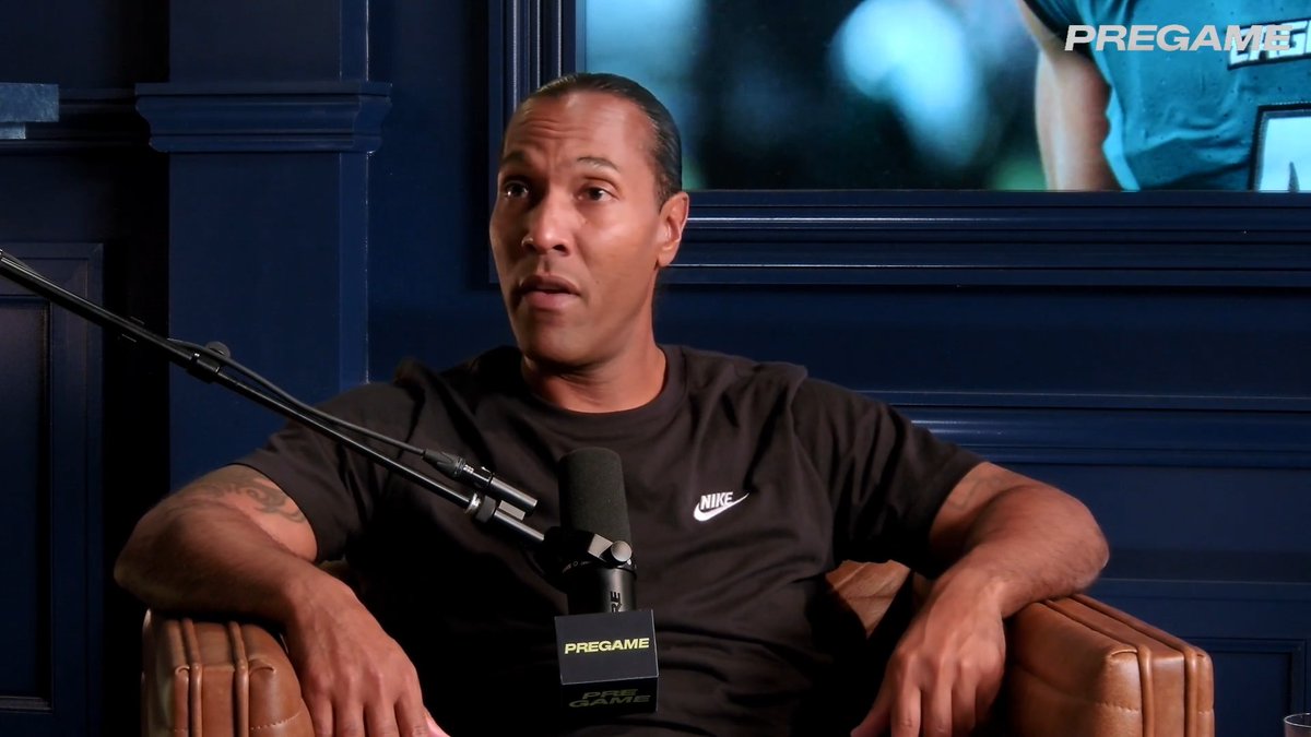 A man wearing a black Nike shirt speaks into a 'PREGAME' branded microphone in a studio setting with dark blue paneled walls.