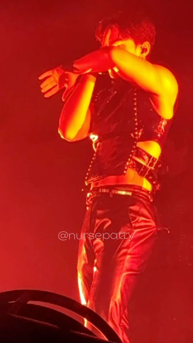 A performer bathed in red stage lighting sings into a microphone while wearing a studded black vest and shiny black pants, with the watermark '@nursepatty' visible.