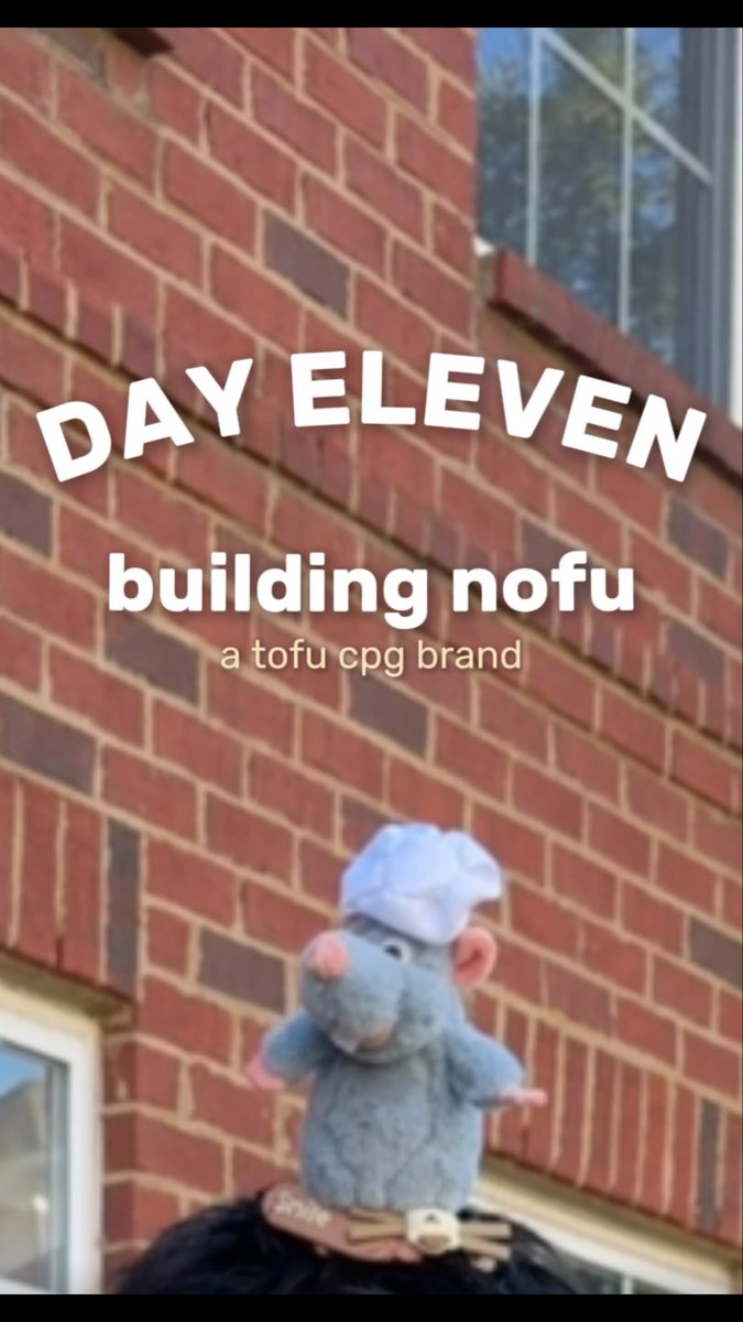 An image of a plush rat toy wearing a chef hat in front of a brick building, with text reading 'DAY ELEVEN building nofu a tofu cpg brand'.