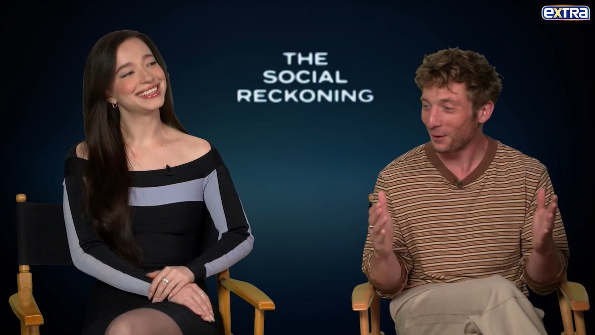 Actors Mike Faist and Adria Arjona sit in director's chairs during an interview for 'extra', smiling and talking, with 'THE SOCIAL RECKONING' displayed on the screen behind them.