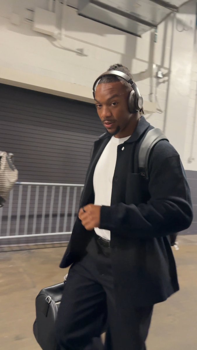 A young man wearing headphones and a black jacket walks through what appears to be an arena tunnel, carrying a bag. The image likely depicts Atlanta Falcons running back Bijan Robinson heading to a primetime game against the New Orleans Saints, as referenced in the accompanying post.