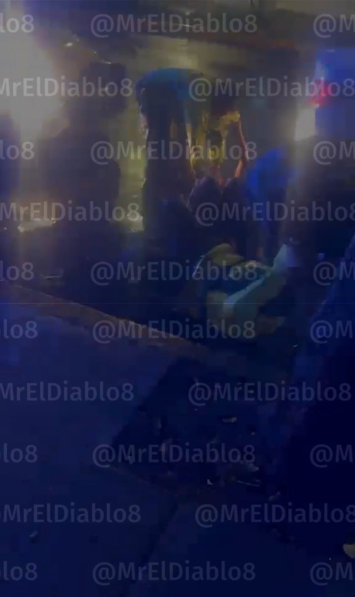 Blurry image showing what appears to be an altercation at night with blue and red lighting, heavily watermarked with "@MrElDiablo8" repeated across the frame. The image relates to the post by depicting the confrontation between a man and a SSC CDMX police officer in the Acoxpa neighborhood of Tlalpan, where the individual reportedly assaulted the uniformed officer after being told he violated traffic regulations.