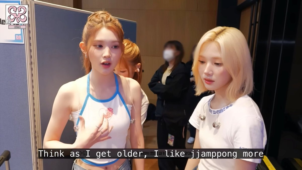 Two young women with reddish and blonde hair wearing white tank tops appear in what looks like a backstage interview, with a subtitle reading "Think as I get older, I like jjamppong more".