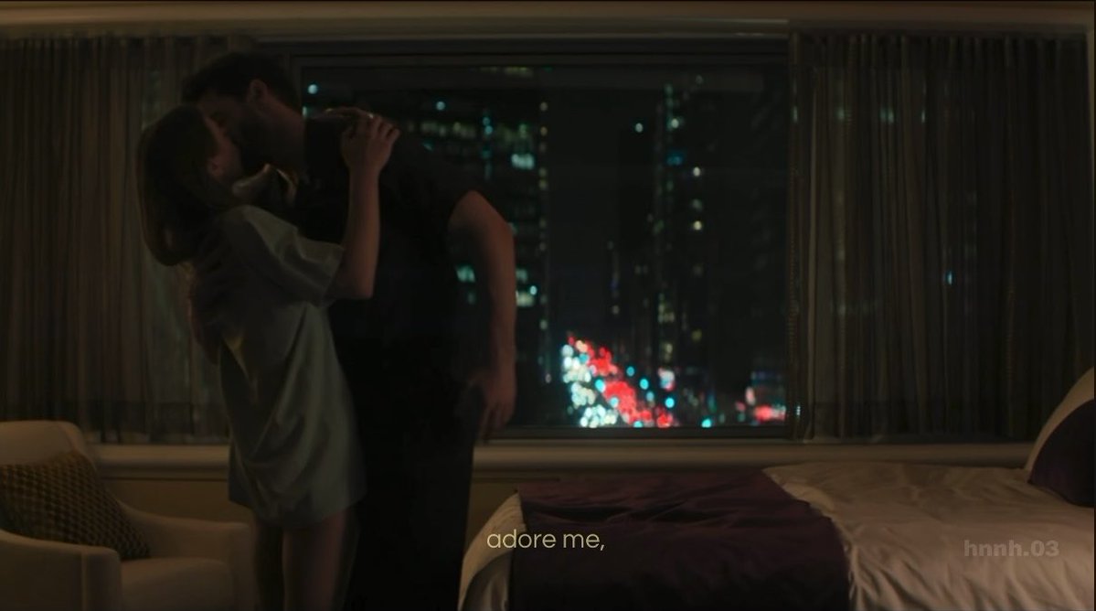 A dimly lit scene of a couple kissing in front of a window with a city skyline at night, with the text 'adore me,' and a watermark 'hnnnh.03'.