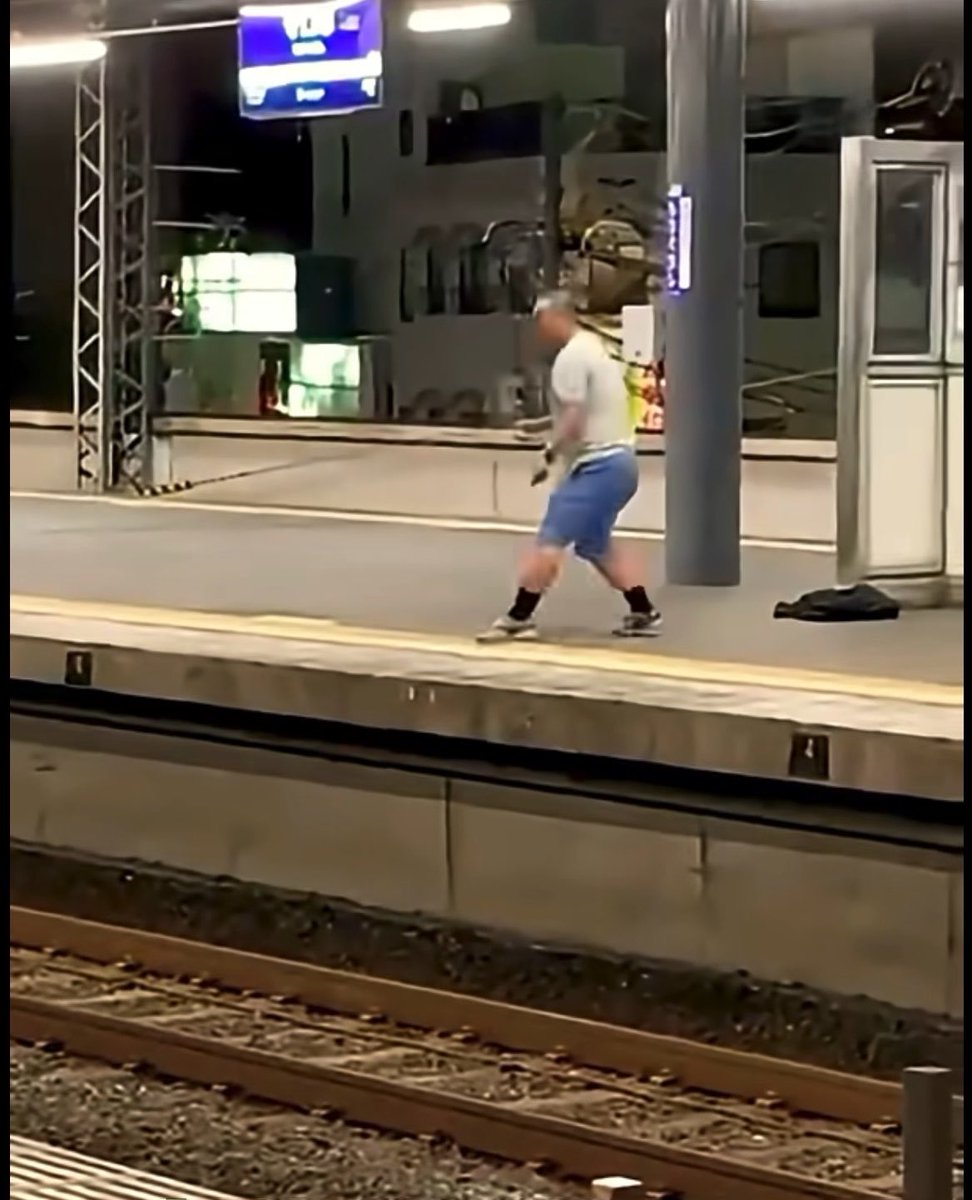 A blurry image of a person walking on a train station platform, viewed from across the tracks.