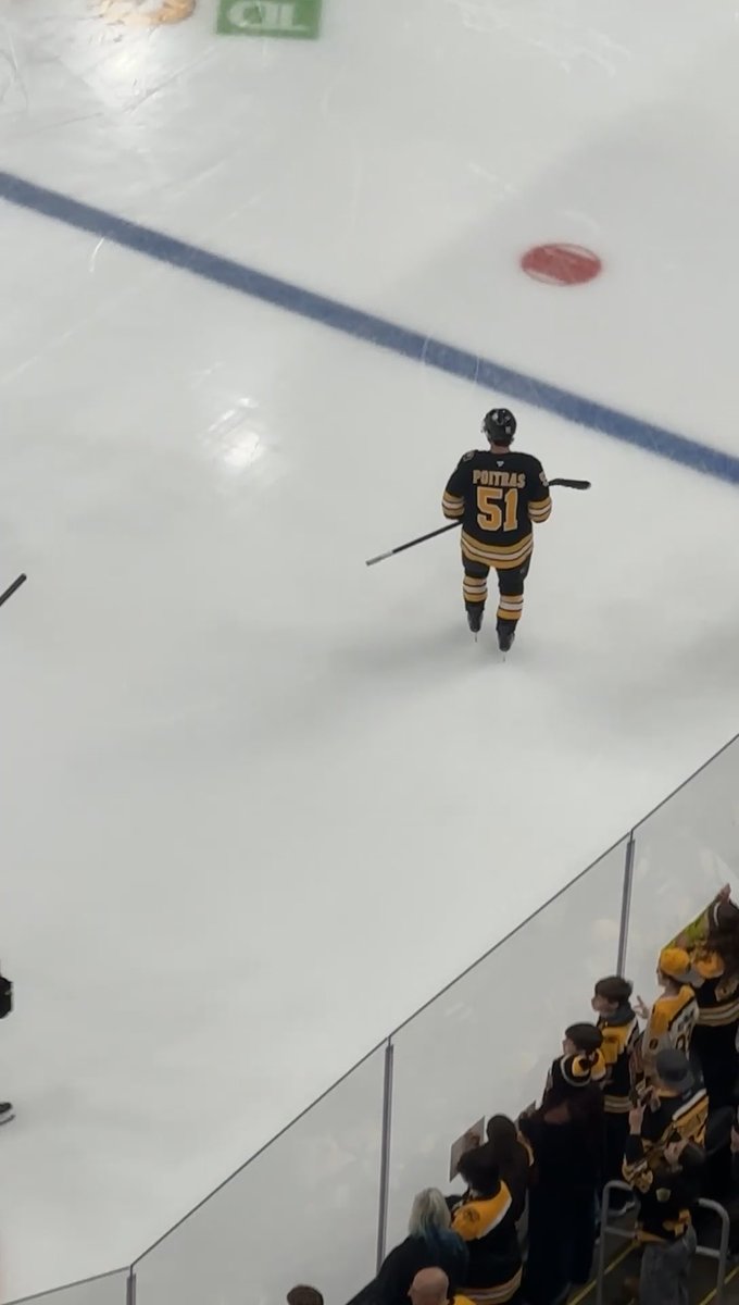 A hockey player wearing a black and yellow jersey with 'POITRAS 51' skates onto an ice rink toward cheering fans wearing matching jerseys behind the glass.