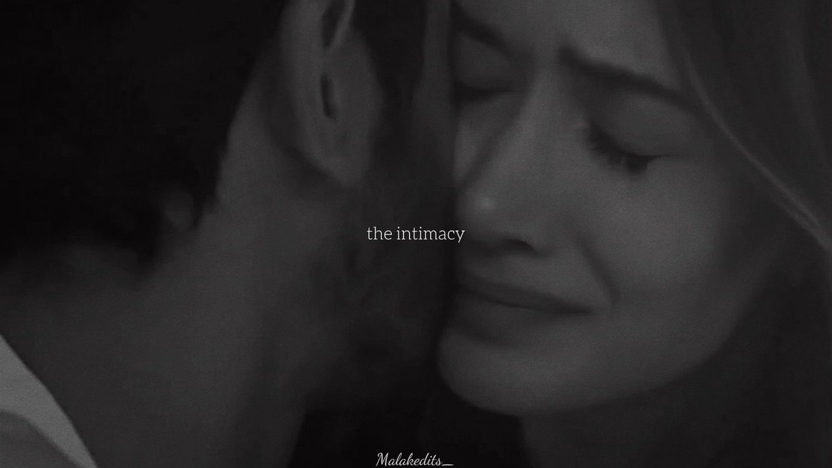 A black and white close-up photograph captures an intimate moment between two people with their eyes closed, with the words 'the intimacy' overlaid in the middle and 'Malakedits_' at the bottom.