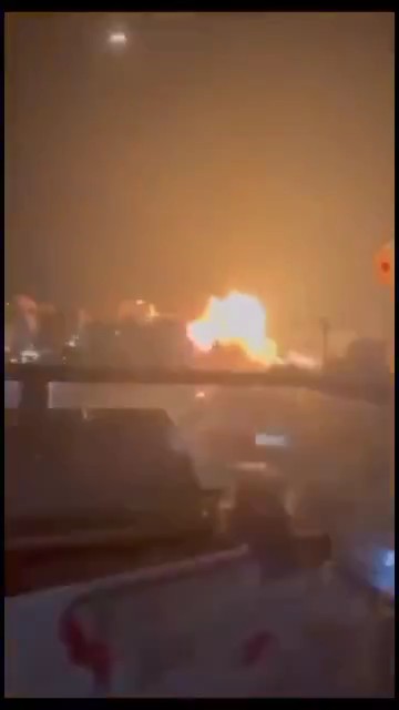 A nighttime view from a residential rooftop shows a large fireball and explosion in the distance, with a faint object visible in the sky above, likely depicting the Houthi missile strike on Riyadh mentioned in the accompanying post.