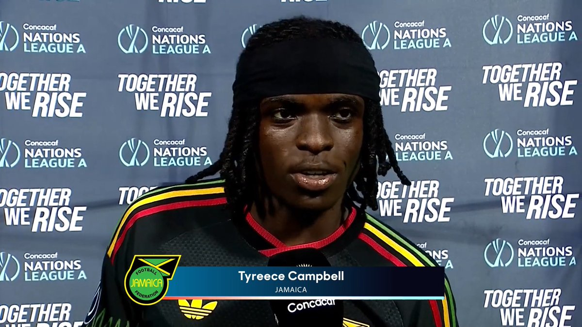 Soccer player Tyreece Campbell of Jamaica wearing a black, green, and yellow jersey speaks into a microphone at a Concacaf Nations League A press event with a 'Together We Rise' backdrop.
