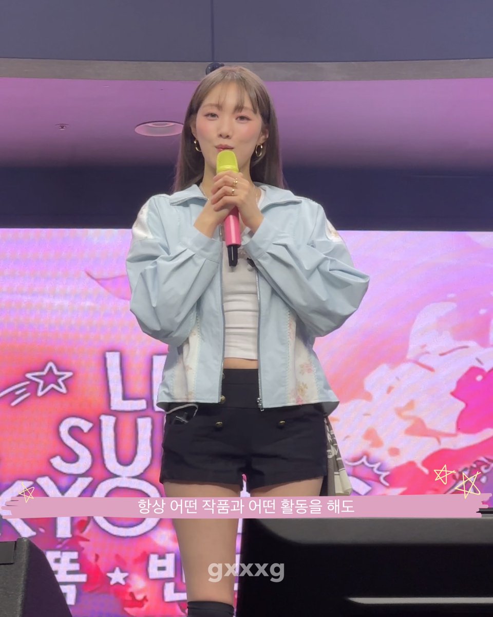 A female performer with bangs and a blue bow holds a microphone while wearing a light blue jacket and black shorts, standing on stage with Korean text '항상 어떤 작품과 어떤 활동을 해도' overlaid at the bottom.