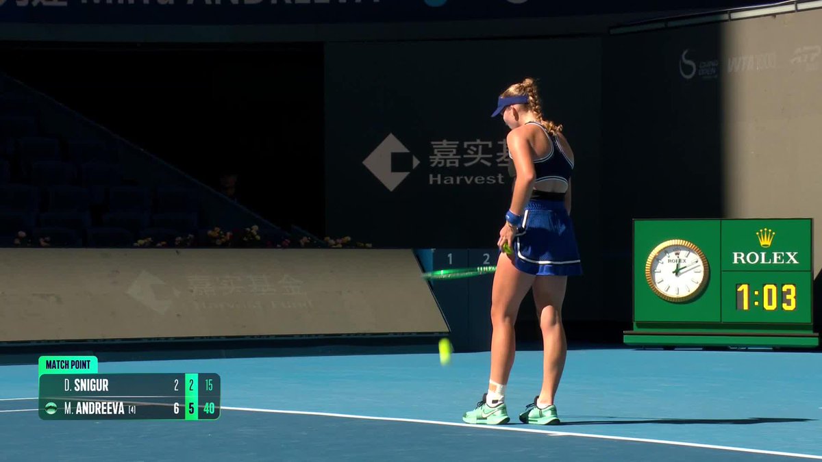 A tennis player in blue attire prepares to serve during a match point, with the scoreboard showing D. Snigur trailing M. Andreeva 2-6, 2-5 (15-40) and a Rolex clock displaying 1:03.