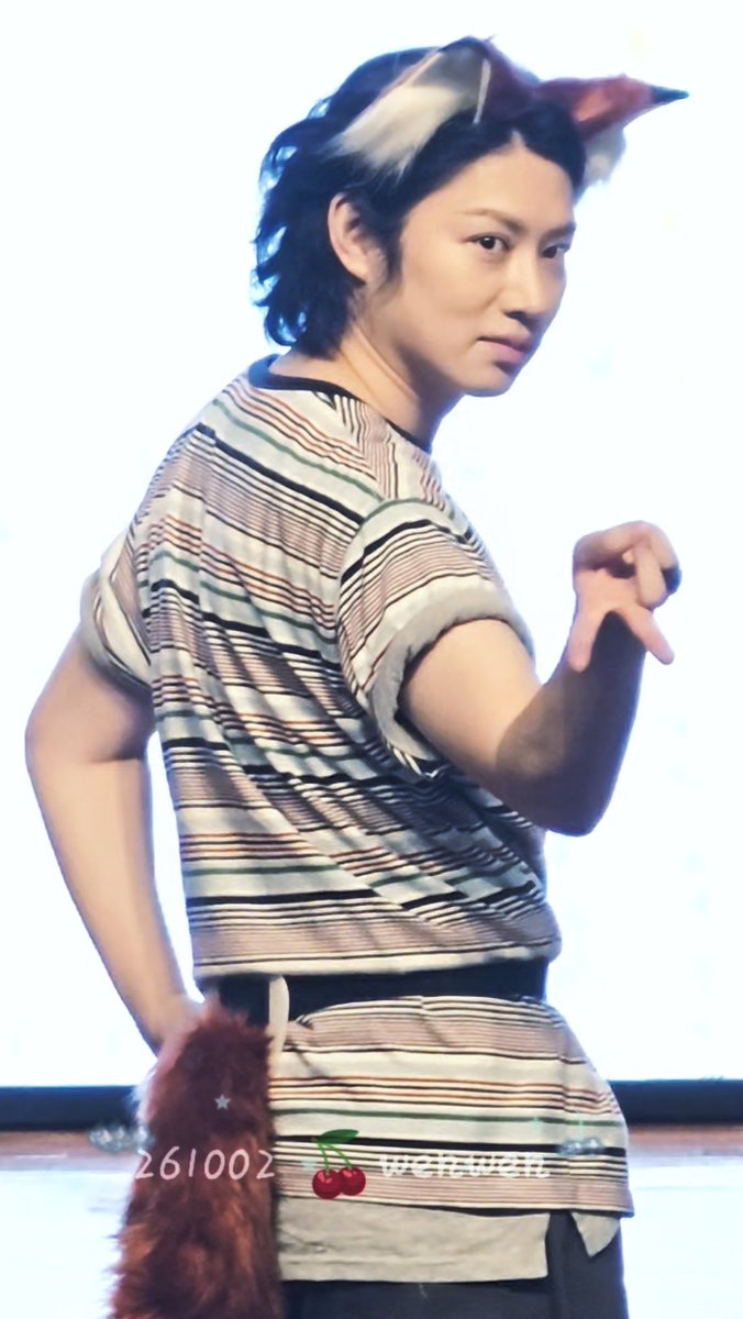 A person wearing a striped shirt, a furry tail, and a furry headband with animal ears, striking a playful pose, with the text '261002' and a cherry emoji visible at the bottom.