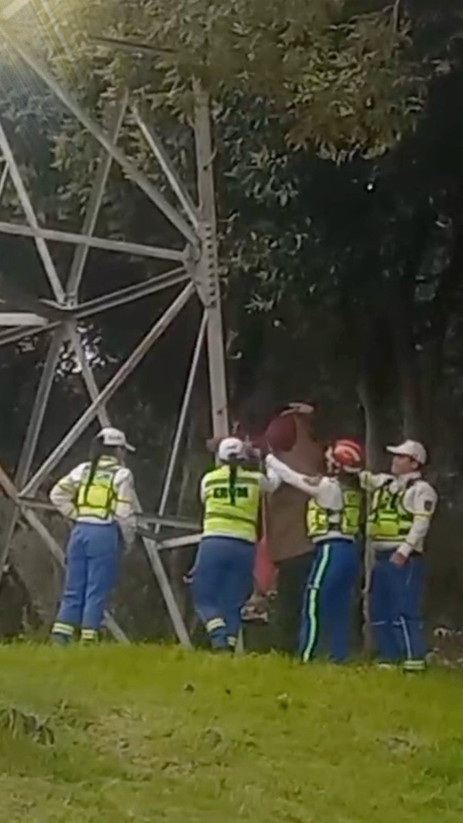 Four emergency responders in high-visibility vests and helmets assist a woman in a red top who appears to be stranded on a tall metal electrical tower at night. The scene aligns with the post describing ERUM and SSC-CDMX personnel rescuing a woman who climbed an electrical tower in the Héroes de Padierna neighborhood of Tlalpan, Mexico City.